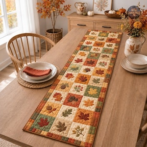 May include: A rectangular quilted table runner featuring a patchwork design of autumn-themed squares. The fabric squares display embroidered motifs of maple leaves, oak leaves, acorns, pinecones, and berries in shades of orange, red, green, and tan.