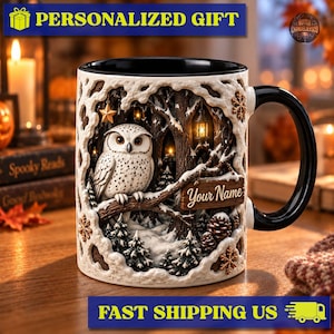 Puede incluir: Una taza de cerámica con asa e interior negros, que presenta una escena de bosque nevado con un búho blanco posado en una rama, una linterna brillante, pinos y un letrero de madera con el texto Your Name, decorado con copos dorados.