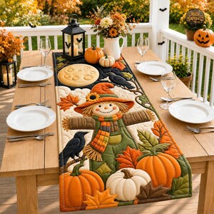 Könnte beinhalten: Ein gesteppter Tischläufer mit einer zentralen Vogelscheuchen-Applikation, die einen Hut und Schal trägt, umgeben von orangefarbenen Kürbissen, Herbstblättern und schwarzen Krähen. Das Design zeigt einen Vollmond und cremefarbene Wolken.