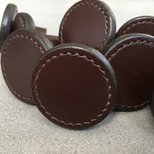 Puede incluir: Primer plano de tiradores de cajones de cuero marrón con borde cosido.