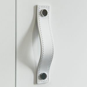 May include: White leather cabinet pull with a curved design and two silver metal screws.