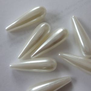 Puede incluir: Un grupo de seis cuentas blancas nacaradas en forma de lágrima. Las cuentas son lisas y brillantes.