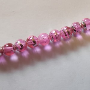 May include: A strand of pink glass beads with silver flecks. The beads are round and have a glossy finish.