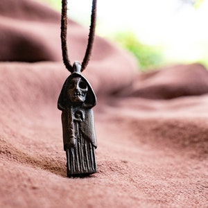 May include: A dark brown leather cord necklace with a detailed metal pendant depicting a hooded figure with a skull face.