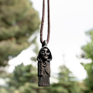 May include: A dark brown leather cord necklace with a pendant featuring a skeletal figure wearing a hooded robe.