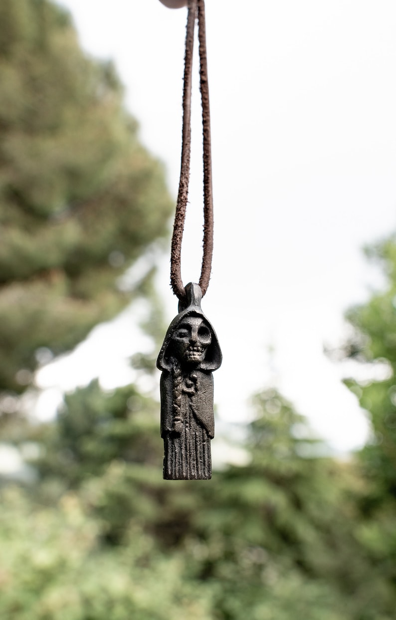 May include: A dark brown leather cord necklace with a pendant featuring a skeletal figure wearing a hooded robe.