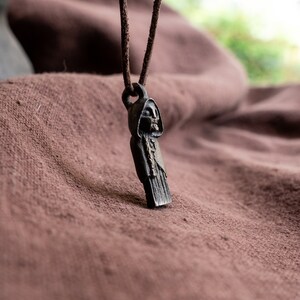 May include: A black metal pendant necklace featuring a hooded figure with a skeletal face. The pendant is hanging on a brown leather cord.