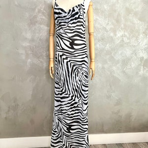 May include: A floor-length dress with a zebra print in black and white. The dress has thin spaghetti straps and a cowl neckline. The dress is displayed on a mannequin with wooden arms and a cork head.