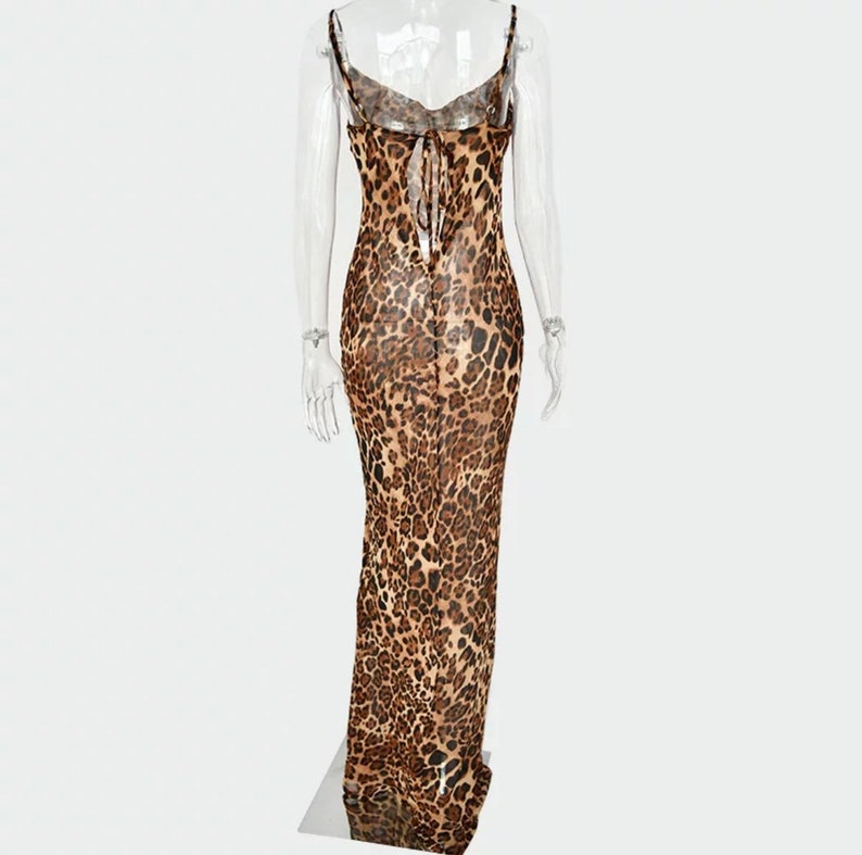 May include: A long, leopard print dress with spaghetti straps and a low back. The dress features a flowing silhouette and a tie detail at the upper back. The fabric has a brown and black spotted pattern.
