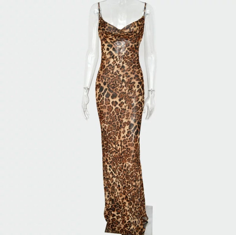 May include: A floor-length dress with a cowl neckline and spaghetti straps. The dress features a brown and black leopard print pattern. The dress is made of a sheer fabric.