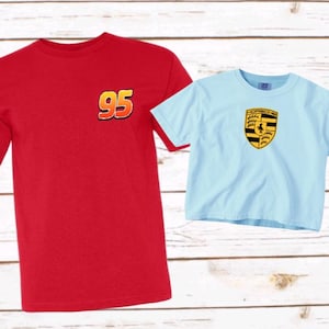 May include: A red short-sleeve t-shirt featuring the number 95 in yellow and orange on the chest, paired with a light blue short-sleeve t-shirt displaying a yellow, black, and red crest logo on the center of the chest.