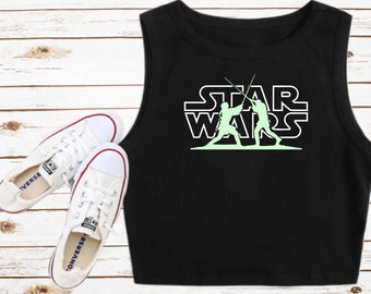 Könnte beinhalten: Schwarzes ärmelloses Crop-Top mit einem weißen Umriss der Worte "STAR WARS" und einer grünen Silhouette von zwei Figuren, die mit Lichtschwertern kämpfen.