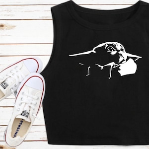 May include: Black crop top featuring a white graphic of a character from a popular science fiction franchise. The top is sleeveless and has a round neckline. White canvas sneakers with red accents are also in the image.