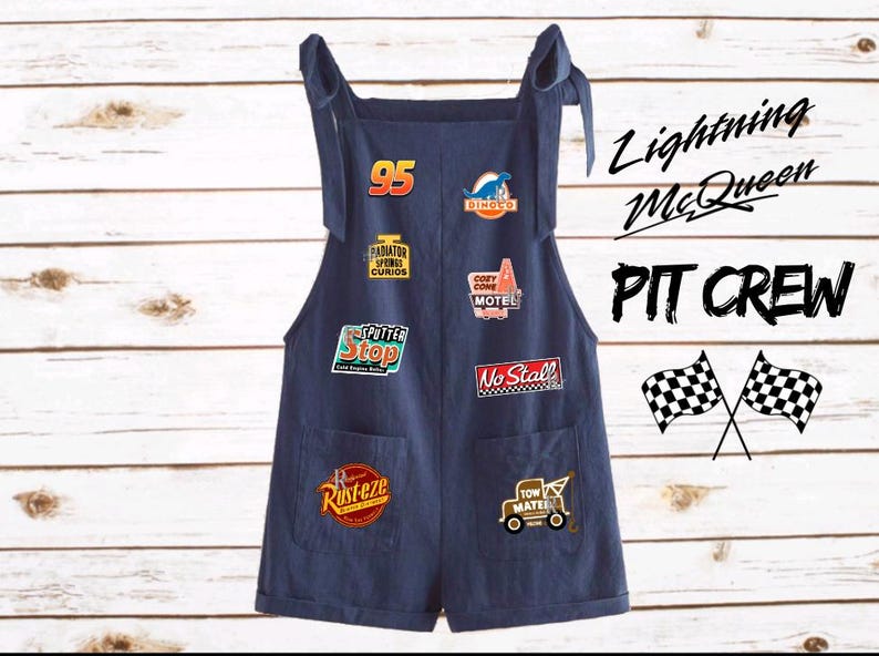 Puede incluir: Mono vaquero azul oscuro con m&uacute;ltiples parches con texto y gr&aacute;ficos. Los parches incluyen "95", "Dinoco", "Radiator Springs Curios", "Cozy Cone Motel", "Sputter Stop", "Rusteze", "No Stall" y una gr&uacute;a. Tambi&eacute;n son visibles las palabras "Lightning McQueen" y "PIT CREW".