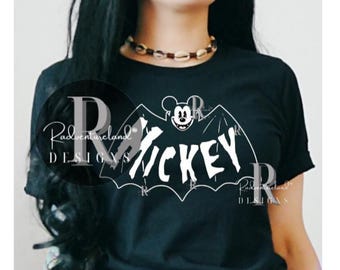 May include: A black short-sleeve t-shirt featuring a white graphic of a bat with the head of Mickey Mouse and the text "MICKEY" in a jagged font. The design includes a watermark logo that reads "Radventureland DESIGNS" in white text.