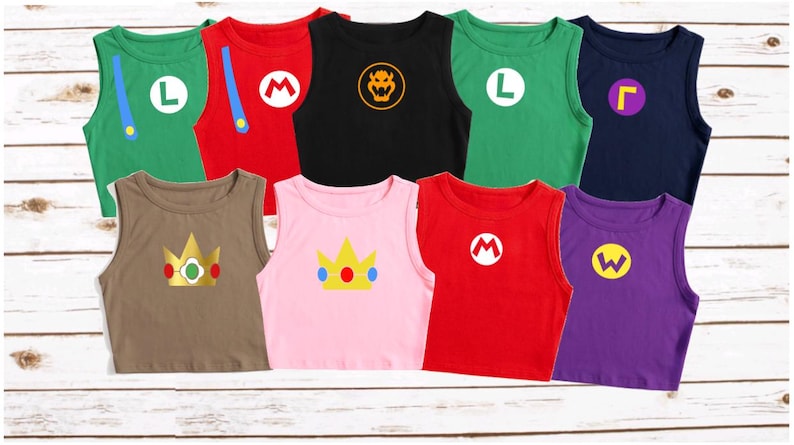May include: A collection of sleeveless shirts in various colors, each featuring a different character design. The shirts include green with a white "L", red with a white "M", black with a Bowser symbol, and more. The shirts are displayed on a light wood surface.