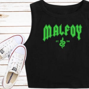May include: Black sleeveless crop top with a green graphic print of the word "MALFOY" in a gothic font. The graphic also includes a green snake and the text "EST. 1980".