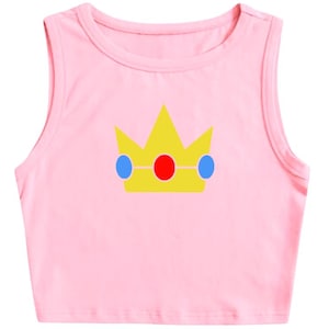 May include: A light pink crop top with a yellow crown graphic. The crown has a red gem in the center and blue gems on either side. The top is sleeveless with a round neckline.