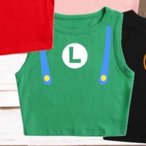 May include: Green crop top with a white "L" emblem, blue suspenders, and yellow accents. The sleeveless shirt is part of a costume set. Other shirts in the image are red, pink, and black.