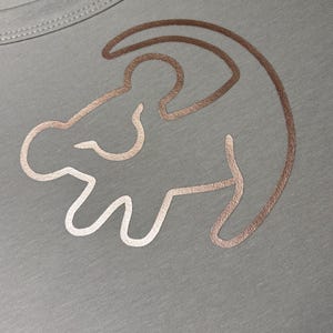 May include: A light gray t-shirt with a gold outline of Simba from The Lion King.