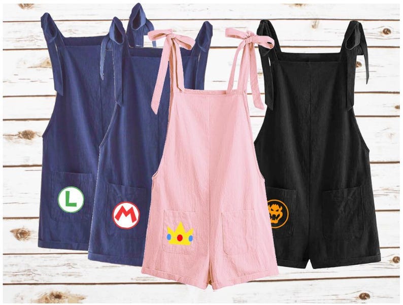 May include: Four pairs of short overalls in navy blue, pink, and black. Each pair has a pocket with a character emblem: a green "L", a red "M", a yellow crown, and a yellow Bowser emblem. The straps tie at the shoulders.