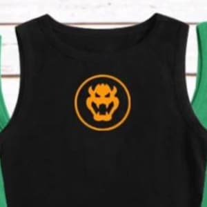 May include: Black tank top with a round orange Bowser logo. The sleeveless shirt has a crew neck and is centered in the image. Two other tank tops, one green and one blue, are partially visible on either side of the black shirt.
