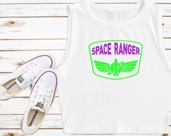 Könnte beinhalten: Weißes Tanktop mit einem grünen und violetten "Space Ranger" Patch mit einem Raumschiff und Flügeln.