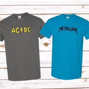 May include: A dark gray short-sleeve t-shirt with the yellow text AC/DC and a bright blue short-sleeve t-shirt with the black text METALLICA printed on the chest. Both shirts feature a crew neckline and a standard fit design for casual wear.