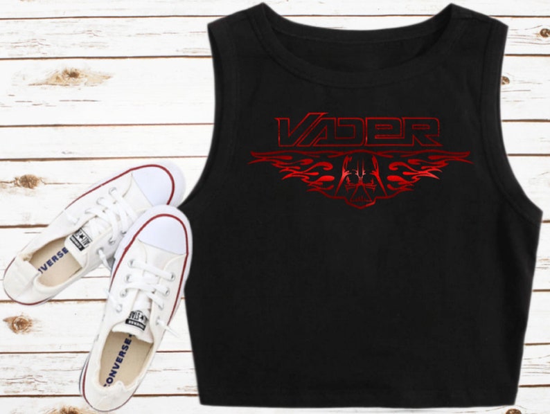K&ouml;nnte beinhalten: Schwarzes &auml;rmelloses Crop-Top mit einer roten Grafik des Wortes "VADER" mit Flammen und einem Darth-Vader-Helm-Design.