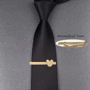 May include: A gold tie clip with a Mickey Mouse head design. The tie clip is on a black tie.