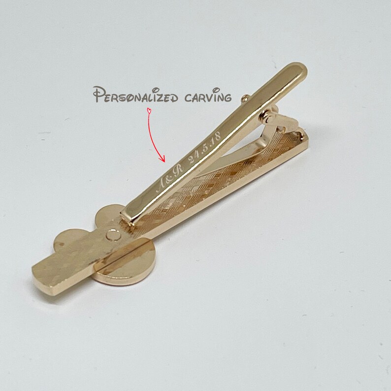May include: Gold-toned tie clip with a clover design. The clip has a personalized inscription that reads "A&R 24.5.18".