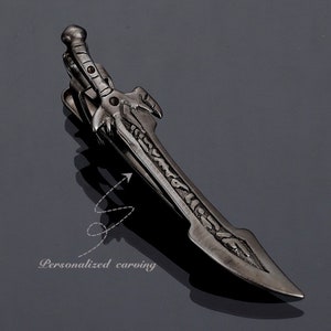 May include: A dark gray metal tie clip in the shape of a sword. The clip features intricate detailing on the blade and hilt, with the words "Personalized carving" in the lower left corner.