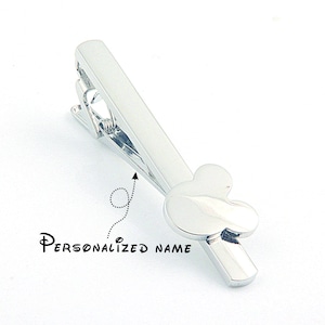 May include: Silver tie clip featuring a Mickey Mouse head design. The tie clip has a spring-loaded clasp and can be personalised with a name.