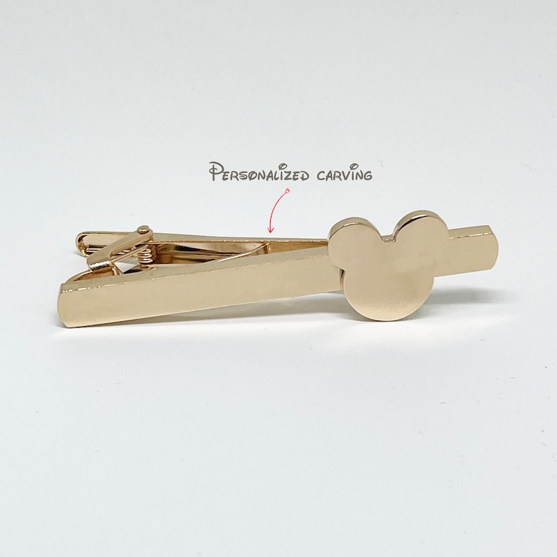 May include: Gold-toned tie clip with a Mickey Mouse head design. The clip has a personalized carving area.