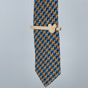 May include: A gold tie clip with a Mickey Mouse head design. The tie clip is on a blue and yellow patterned tie.