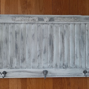 May include: A white painted wooden wall mounted coat rack with five hooks. The rack is made from reclaimed wood with a distressed finish.