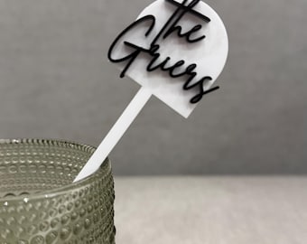 May include: White acrylic drink stirrer with a black inscription that reads "The Gruers".
