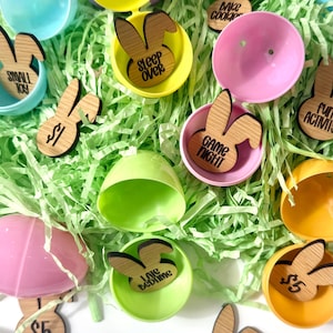 May include: A collection of plastic Easter eggs filled with wooden bunny-shaped tags. The tags have different phrases written on them, such as "Game Night", "Sleep Over", "Sweet Treat", and "Bake Cookies".