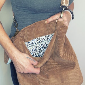May include: A brown corduroy tote bag with a leopard print lining. The bag has a long strap and a metal clasp.