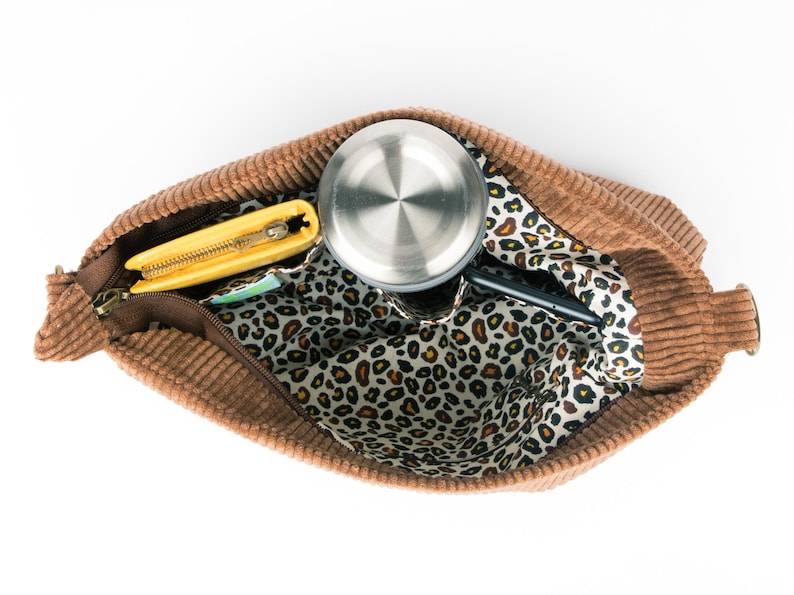 May include: A brown corduroy tote bag with a leopard print lining. The bag is open and contains a yellow wallet, a silver water bottle, and a black phone.