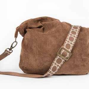 May include: A brown corduroy tote bag with a white and brown patterned strap and a brass buckle.