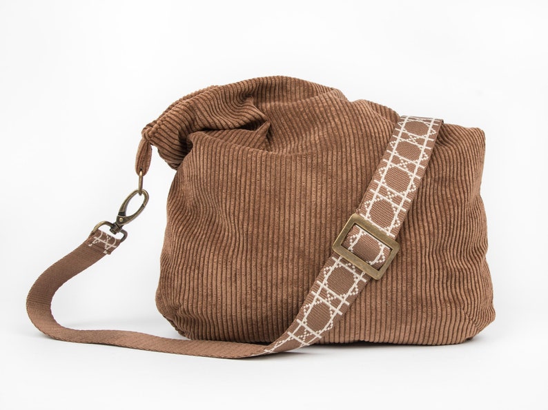 May include: A brown corduroy tote bag with a white and brown patterned strap and a brass buckle.