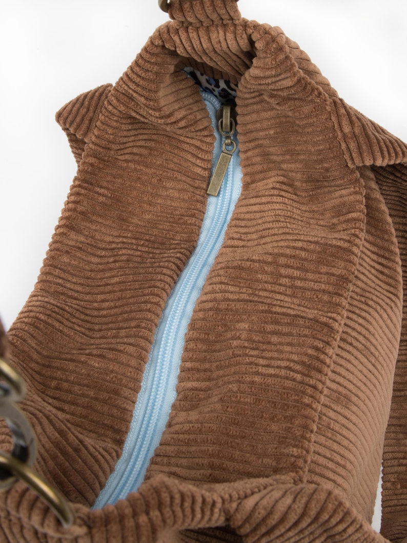 May include: A brown corduroy tote bag with a blue zipper and a metal clasp. The bag is open and the lining is visible.