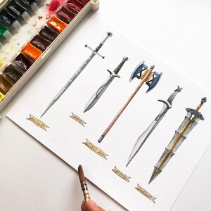 May include: Watercolor painting of five fantasy swords and an axe, each with a unique design and name. The artwork includes a palette of watercolor paints and a paintbrush, suggesting the tools used to create the illustrations.