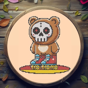 Könnte beinhalten: Kreuzstich-Design eines Bären mit Totenkopfmaske und Rollschuhen. Der Bär ist braun mit einem weißen Totenkopfgesicht und roten Augen. Die Rollschuhe sind rot und blau, in einem hölzernen Stickrahmen.