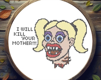 May include: Cross-stitch art in a wooden hoop featuring a cartoon woman with blonde pigtails and a wide open mouth. The text "I WILL KILL YOUR MOTHER!!!" is stitched above the woman's head. The background is a wooden surface.