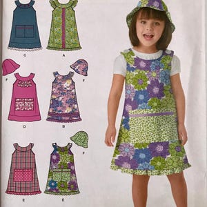 May include: Simplicity sewing pattern 1815A for a sleeveless dress and hat in sizes 3, 4, 5, 6, 7, 8. The package displays illustrations of six variations of the dress and hat, featuring floral, plaid, and solid fabrics with pockets and ruffles.