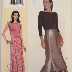 May include: A vintage sewing pattern titled "7025" with illustrations of two women wearing different outfits. One woman is in a pink top and floral skirt, the other in a brown top and a layered skirt. The text "TODAY'S FIT" is visible.