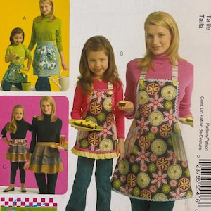 May include: McCall's Fashion Accessories sewing pattern. The package features images of aprons with floral and striped designs. The aprons are modeled by women and children. The text on the package includes "MP399" and "the apron lady."