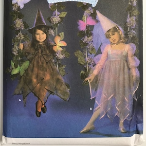 May include: Simplicity sewing pattern for children's costumes. The cover features two children dressed as a witch and a fairy. The witch costume is brown with a pointed hat, and the fairy costume is pink with a pointed hat. The text reads "Costumes for kids".